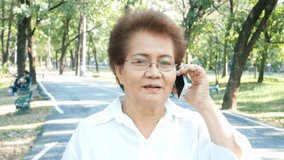 Elderly asian woman using phone for talk at park.