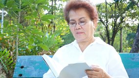 Elderly asian woman reading book at park.