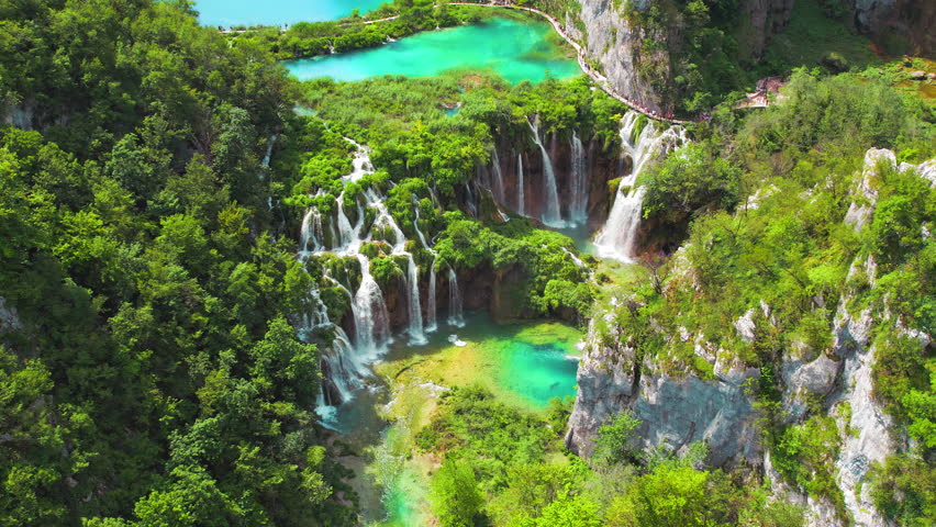 Mountain lake with streams of water and waterfalls. People hiking on narrow path in Plitvice National Park Croatia.