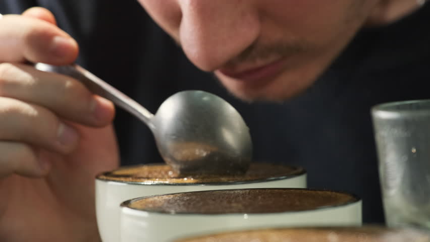 Man assesses texture and balance of coffee in cup with spoon. Inspector draws on sensory experience to provide feedback on quality