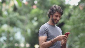 View of a young man with smartphone at daytime in a green park in the city. High quality video.
