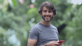 View of a young man with smartphone at daytime in a green park in the city. High quality video.