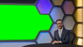 White News Reporter in a dark blue suit is sitting at a table in front of a big green screen, sharing a news. The symmetry of colors is displayed on the screen. News Tv Youtube modern Studio