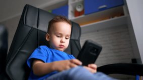 Lovely Caucasian child using a smartphone. Focused kid watches video and opens mouth wide. Low angle view.