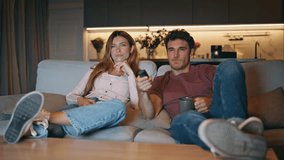 Young pair watching television switching channels at domestic couch. Unshaven man holding remote tv controller at evening. Relaxed couple choosing movie sitting sofa together. Entertainment concept  - Powered by Shutterstock - Get 15% off with code: PIKWIZARD15
