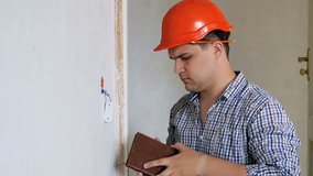 Slow motion video of young handyman making notes in his notebook about house renovation