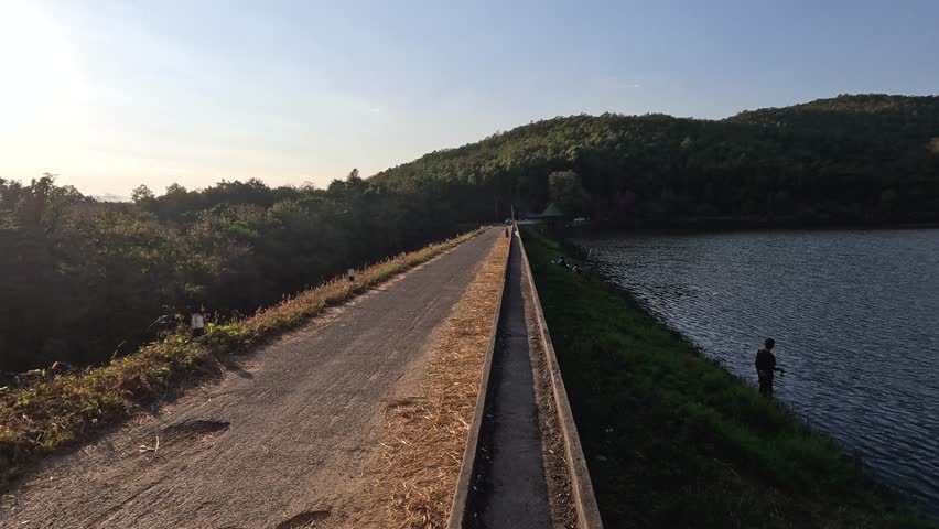 Person walking on dam path by a lake