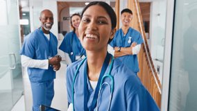 Close up portrait of smiling female doctor or nurse with digital tablet wearing scrubs standing in hospital corridor with multi-cultural team of colleagues in background - shot in real time - Powered by Shutterstock - Get 15% off with code: PIKWIZARD15