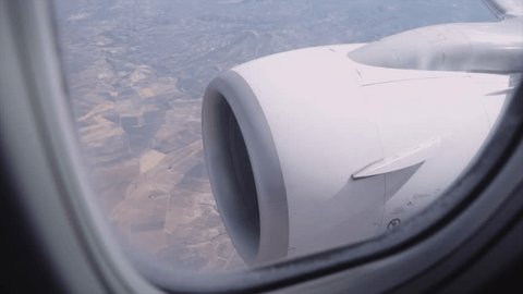 Handheld shot of jet engine and patchwork landscape seen through airplane window Stock Video