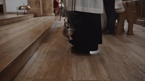 Low section of priest with catholic thurible swinging in slow motion at church