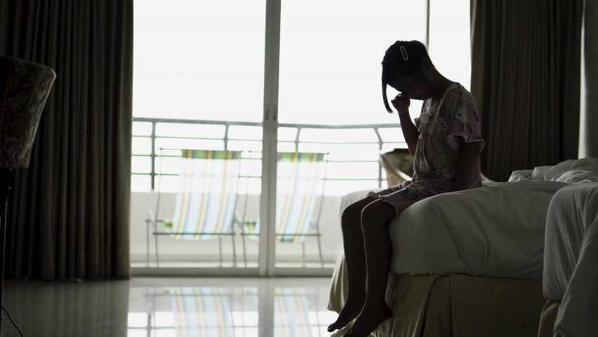 silhouette of a sad little girl sitting in bed at home, family problems. fear and fobies of child. Psychological portrait of scared young girl.	