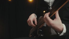 A married elegant guitarist in a black suit plays bass guitar at an evening concert in the spotlight. Close-up. A jazz concert in the rays of concert light on a dark background. Music concert. 4K - Powered by Shutterstock - Get 15% off with code: PIKWIZARD15