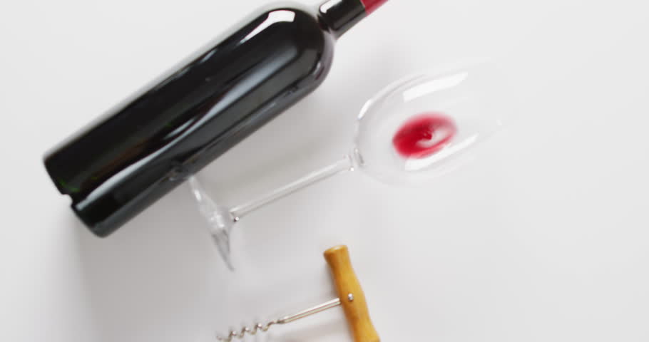 A bottle of red wine lies next to a tipped glass, with copy space. Corkscrew nearby suggests a recent opening or tasting event at home, slow motion.