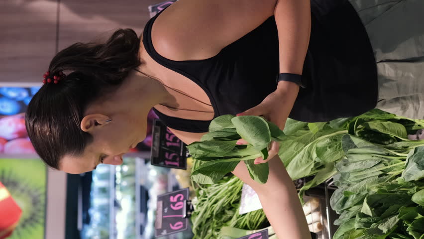 Vertical video. Young woman buying fresh green vegetables at grocery. Choosing from bok choy and spinach, slow motion Royalty-Free Stock Footage #3440760649