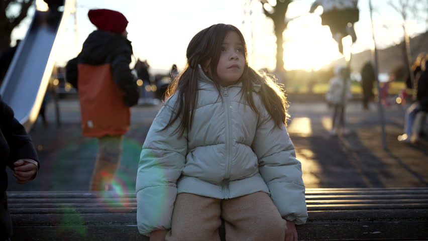 5 year old boy sitting next to 8 year old girl at park bench during sunset winter season time, backlit. Small brother seats next to sister during contemplative tranquil moment outside Royalty-Free Stock Footage #3440797385