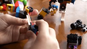A boy is disassembling a colorful vehicle made of interlocking plastic construction toy cubes on a wooden table, a close-up view of hands.