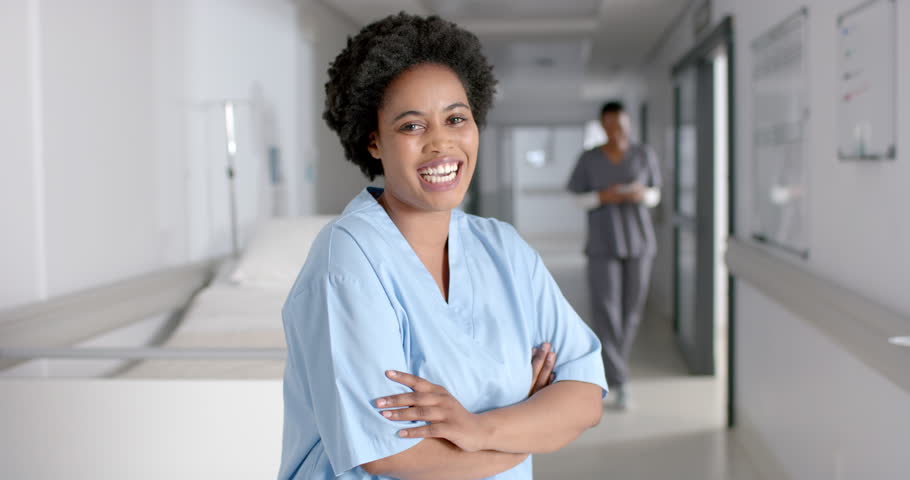 Confident African American nurse stands in a hospital corridor. Her warm smile reflects the compassionate care provided in healthcare settings, slow motion. Royalty-Free Stock Footage #3440820387