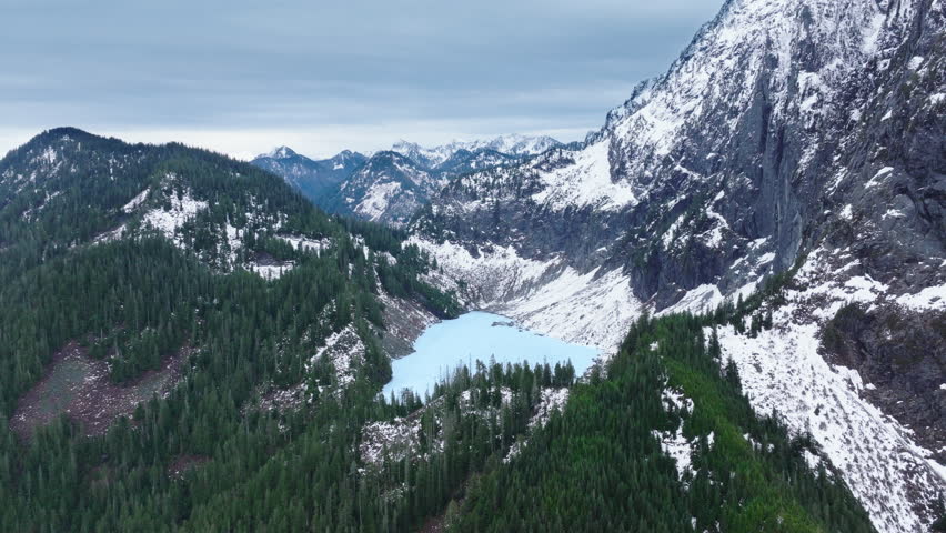 Lake Serene at snowy rocky summit in evergreen forest. Cinematic North Cascades mountains. Washington nature 4K USA. Aerial view high peaks of Mount Index. Mountain landscape panorama on winter day