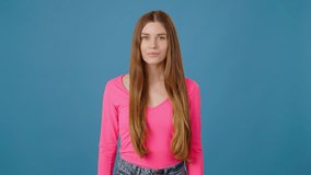 Beauty long haired woman in pink shirt corrects her hairstyle and looking at the camera over blue background. Female appearance concept