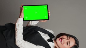 Vertical Video Woman concierge presenting greenscreen display on tablet, showing chromakey template on screen. Receptionist with bow and uniform holding device with blank copyspace layout. Camera A.