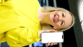 woman dancing in hands with phone white screen advertising space for text joy smile happy eyes bright yellow clothes blonde middle-aged airport waiting 