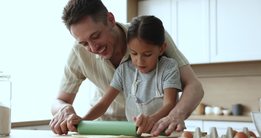 Loving father teach little daughter to flatten homemade dough for holiday pie in cozy kitchen on weekend at home. Loving parent share family recipe and skill with child, upbringing, engaged in cooking Royalty-Free Stock Footage #3440878341