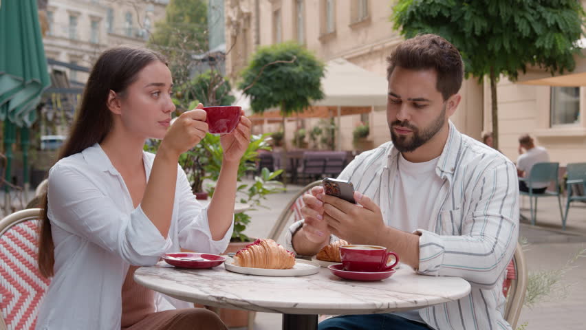 Caucasian couple cafe dissatisfied unhappy woman arms crossed man mobile phone stuck smartphone ignore crisis relationship problem street outside city separation boyfriend girlfriend upset frustration Royalty-Free Stock Footage #3440931263