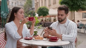Caucasian couple cafe dissatisfied unhappy woman arms crossed man mobile phone stuck smartphone ignore crisis relationship problem street outside city separation boyfriend girlfriend upset frustration - Powered by Shutterstock - Get 15% off with code: PIKWIZARD15
