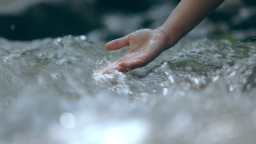 Palm hand touching on clear stream water in the rainforest waterfall. People travel and enjoy with nature. Slow motion shot.