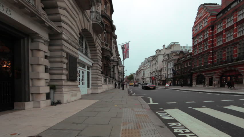 Cars drive down street and people walk across crosswalk in London