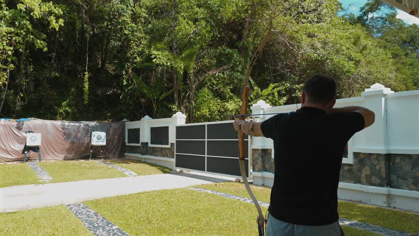 Focused archery man practicing aim and precision at outdoor archery range with multiple targets. Dedication and focus in sports practice.