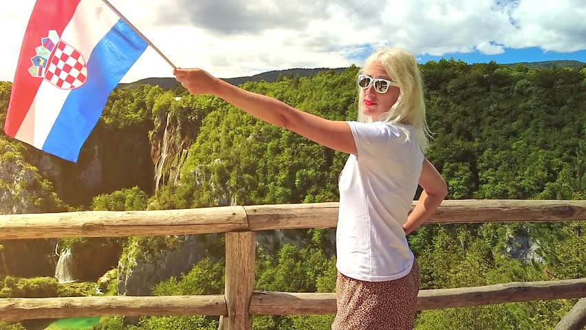 SLOW MOTION: girl with Croatian flag on viewpoint of Plitvice Lakes National Park in Croatia. Sastavci and Veliki Slap waterfalls in Lika region. UNESCO Heritage of Croatia named Plitvicka Jezera