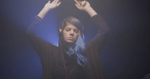 Girl with blue hair and red headphones. Portrait of a lady dancing. Blue beam of light and smoke in the backgorund. Slow motion video recorded at 50fps