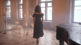 A woman in a black dress is standing in a room next to a piano