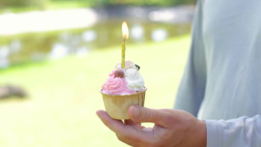 Burning golden candle in dessert. Birthday candle in a cupcake. Celebration of the gender party in the park. Man holding muffin in nature