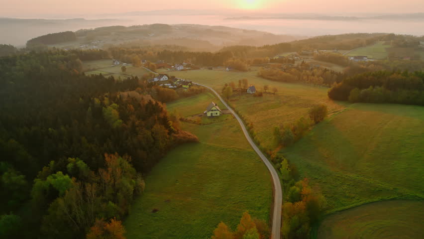Misty morning aerial landscape of the summer countryside. A country road cuts through the mountain village at sunrise. Drone aerial view