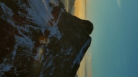 Aerial view of amazing rocky mountains in snow and sunrise sun, Dolomites, Italy. Vertical video