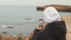 teenage girl shoots video on her phone. A hipster woman takes pictures of a beautiful seascape on her phone. Generation Z. Video shot around. Seascape with a woman. Young girl on the seashore.