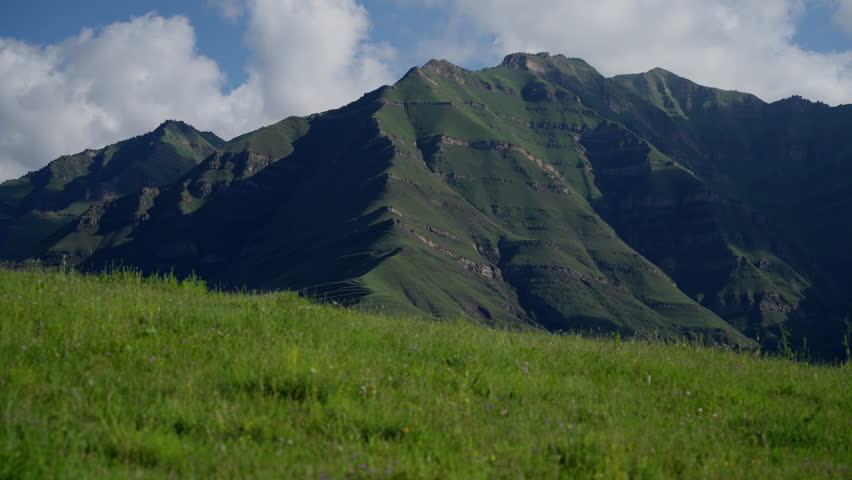Rugged mountain ridges rise above verdant valleys, under a dynamic sky. Dramatic Mountain Ridges and Green Valleys under Cloudy Skies