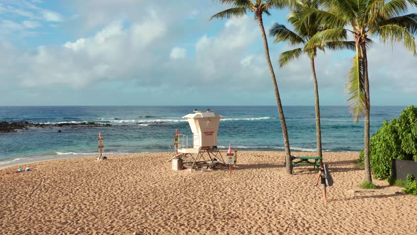 Lifeguard tower on beach in Hawaii in beautiful sunset or sunrise light. Man with guitar walking by Palm trees