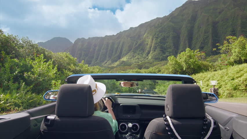 Back view of modern blue convertible car driving away. Driver woman enjoying majestic jungle mountain views. Woman travels Oahu island on summer vacation. Happy tourist in blue convertible car Hawaii Royalty-Free Stock Footage #3441516839
