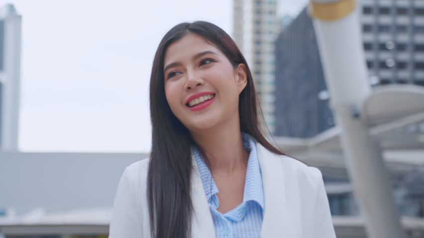 Asian youg beautiful businesswoman standing outdoor in modern city. Attractive employee girl worker feel happy and confident walking around outside the office. Job application and recruitment concept.