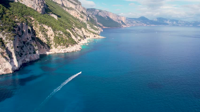 Aerial drone view on white sand Cala Goloritze in Orosei Gulf of Sardegna. Warm turquoise sea, small beach and boats with green mountains on the Sardinia island.