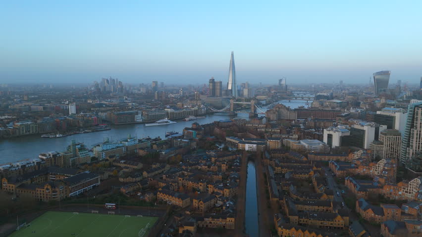 A sweeping drone view of the London skyline featuring The Shard and a wide Thames River, Tower of London under a clear sky in the soft light of early morning. London, UK 