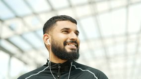 Happy adult bearded athlete relaxing with closed eyes standing in urban city stadium. Smiling handsome sportsman in headphones rests, feels calm, breathes deeply and enjoys listening to music Close up - Powered by Shutterstock - Get 15% off with code: PIKWIZARD15