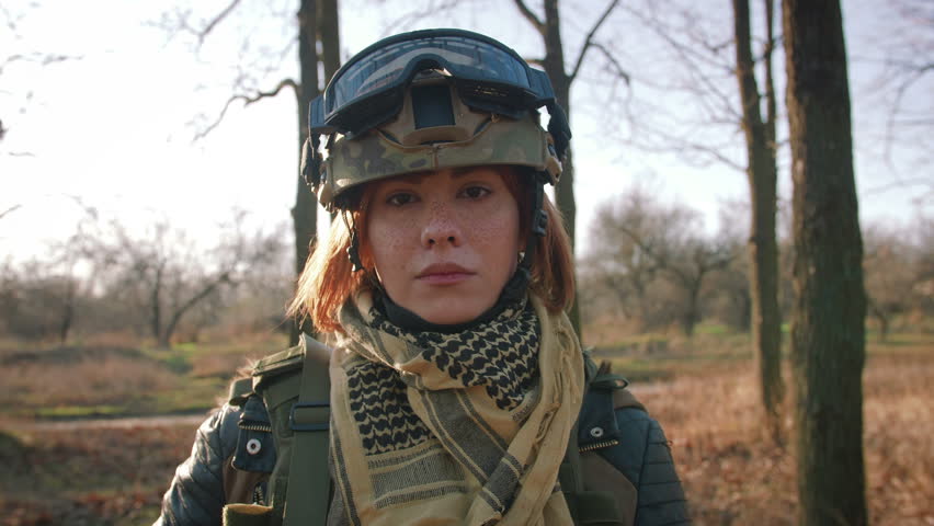 Young pretty redhead woman in military uniform armed with rifle at the battlefield area