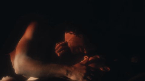 Passionate lovers lying on bed and kissing in dark room with fire flames projection Stock Video