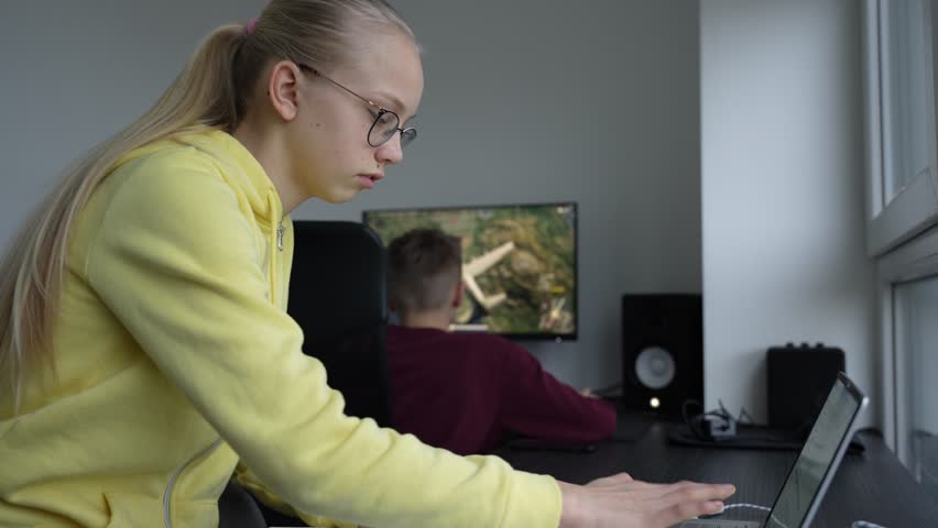 Young sad, tired, depressed girl doing her homework. Young schoolgirl don't understand the task. Disappointed girl puts her hands on the face. Boy plays computer games in the background. Royalty-Free Stock Footage #3441783011