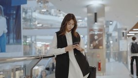 A woman is standing in a mall, checking her phone. She is wearing a stylish hat and formal wear, showcasing the latest fashion design trends