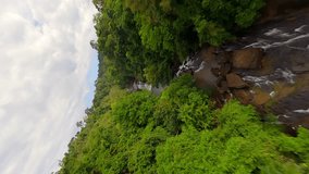 Vertical video. Dynamic FPV flight over tropical waterfall and river in the lush jungle in Thailand.